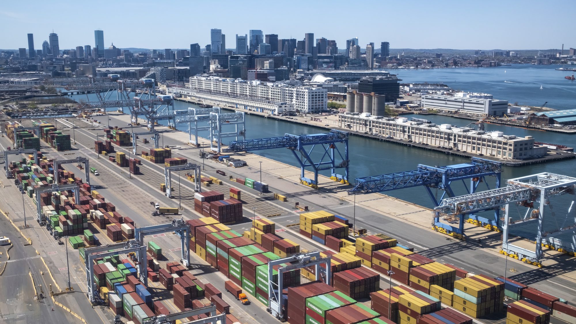 Aerial view of shipping containers and gantry cranes at a waterfront container terminal.