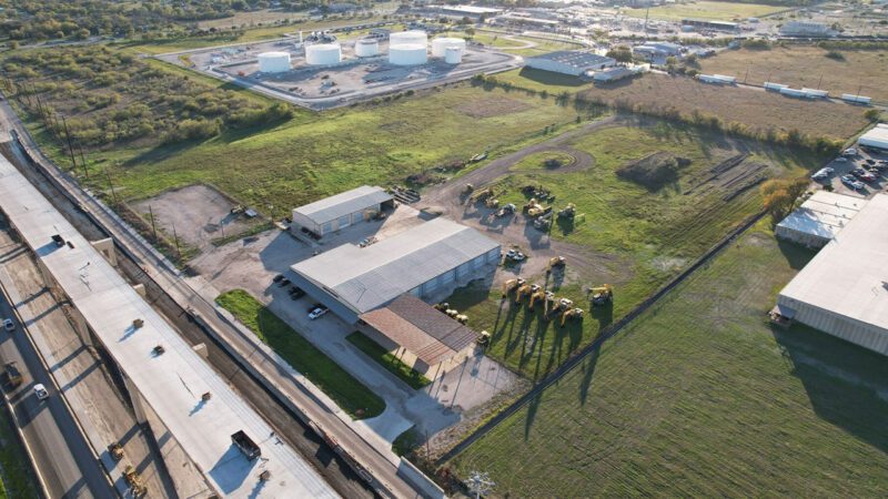 Aerial view of a warehouse and fenced outdoor storage yard fronting a highway